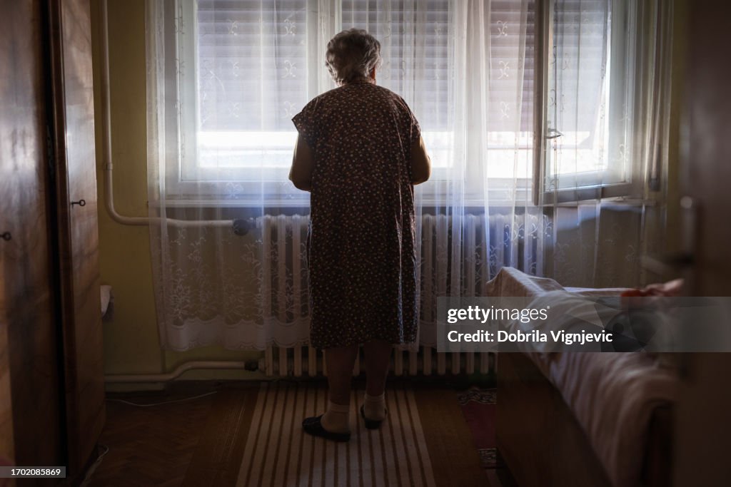 Senior woman looking through window curtain