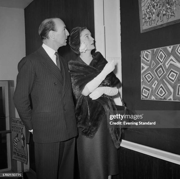 Parliamentary Under-Secretary of State for the Colonies John Profumo with his wife, actress Valerie Hobson viewing Nigerian paintings at The Tea...