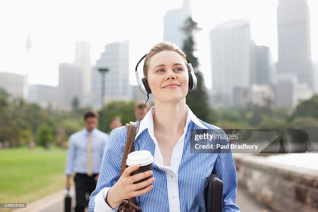 Donna d'affari ascoltando le cuffie e portare il caffè