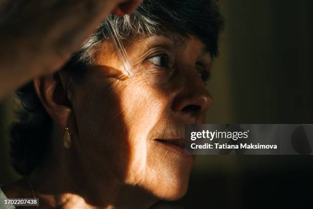 close-up of an elderly woman with a pipette near her skin. a streak of light on the cheek. concept of elderly skin care and natural beauty. - woman portrait skin stock-fotos und bilder