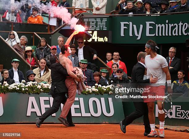 Rafael Nadal of Spain looks on as security guards restrain a protester after he lit a flare and ran on court before the start of a game in the Men's...