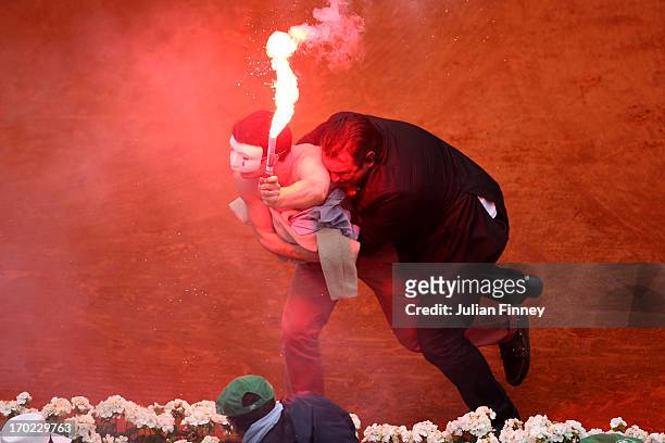 Security guard restrains a protester after he lit a flare and ran on court before the start of a game in the Men's Singles final match between Rafael...