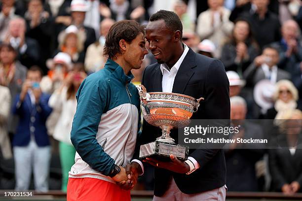 Rafael Nadal of Spain is presented with the Coupe des Mousquetaires trophy by Usian Bolt after the men's singles final against David Ferrer of Spain...