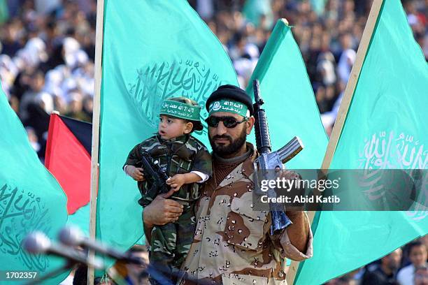 Palestinian activist of the Islamic militant group Hamas holds a gun and carry a child during a rally to mark the 15th anniversary of the group's...