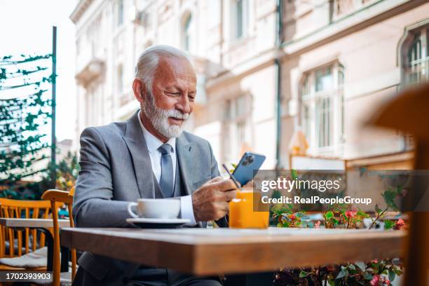 ein älterer geschäftsmann, der fröhlich auf sein mobiltelefon schaut - real businessman isolated no smile stock-fotos und bilder