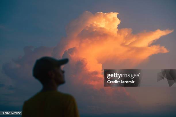 silhouete of man with cap while looking at storm clouds - bright colours stock pictures, royalty-free photos & images