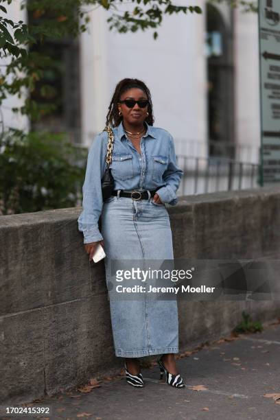 Guest is seen Outside Peter Do show wearing golden earrings, golden necklaces, black Bottega Veneta pouch with golden strap, blue denim shirt with...