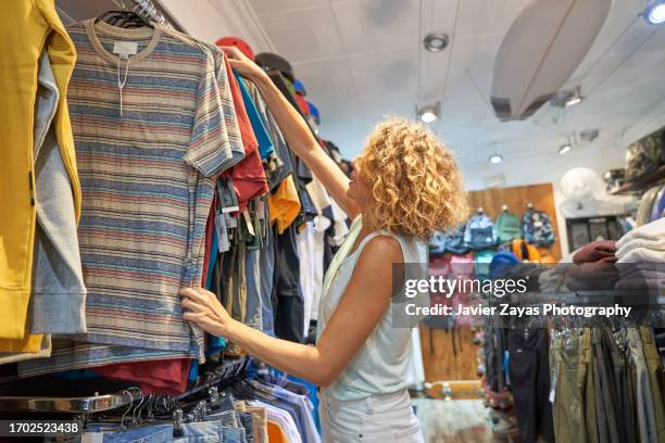 female clothing store owner arranging items of stock along clothing racks and keeping the shop tidy - pre labeled stockfoto's en -beelden