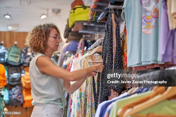 female clothing store owner arranging items of stock along clothing racks and keeping the shop tidy - pre labeled 個照片及圖片檔