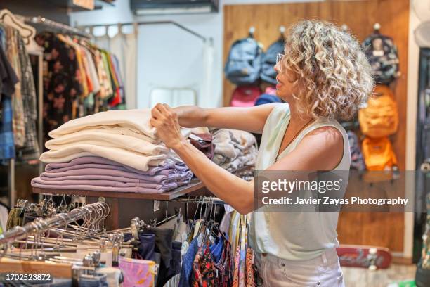 female clothing store owner arranging items of stock along clothing racks and keeping the shop tidy - pre labeled 個照片及圖片檔