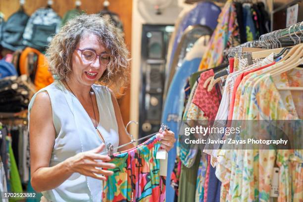 female clothing store owner arranging items of stock along clothing racks and keeping the shop tidy - pre labeled stockfoto's en -beelden