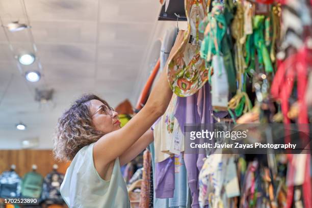 female clothing store owner arranging items of stock along clothing racks and keeping the shop tidy - pre labeled stockfoto's en -beelden