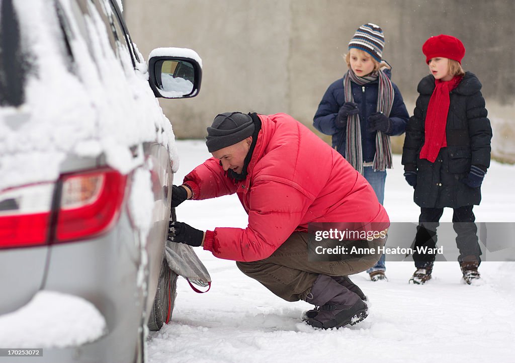 Father fitting a snow sock on family car