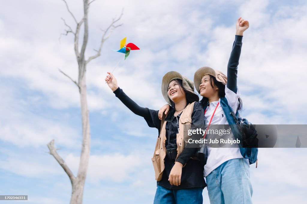 Two teenage twin sisters were playing in the grass holding flowers and paper mills.