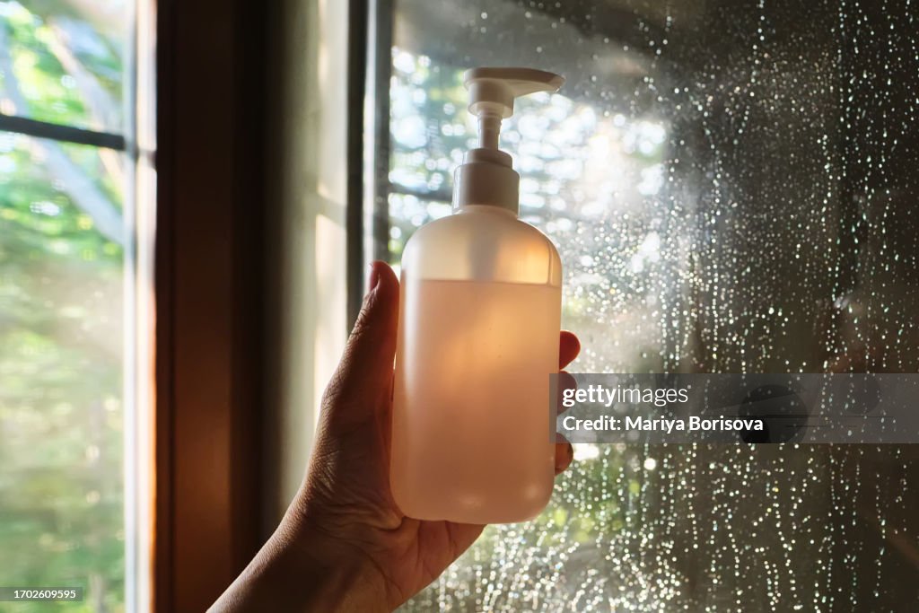 A hand holds shower gel on the background of a shower stall.