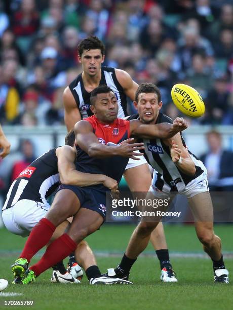 David Rodan of the Demons handballs whilst being tackled by Ben Kennedy and Luke Ball of the Magpies during the round 11 AFL match between the...