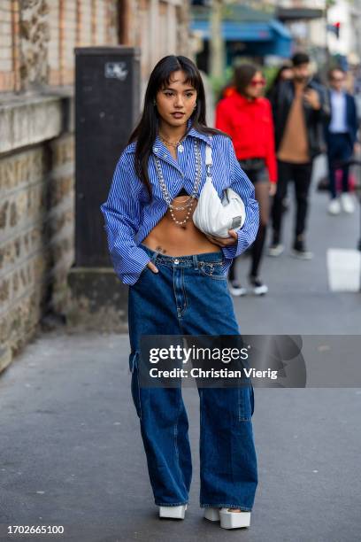 Guest wears white bag, blue white striped button shirt, denim jeans outside Victoria/Tomas during the Womenswear Spring/Summer 2024 as part of Paris...