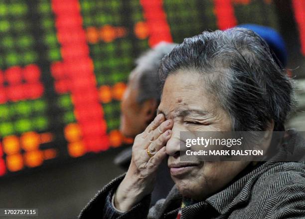 An elderly Chinese investor gestures in front of a stock price board showing falling prices at a private securities firm in Shanghai, 17 January...