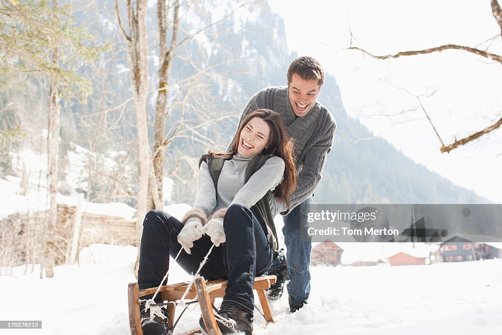 Man pushing woman on sled in snowy woods