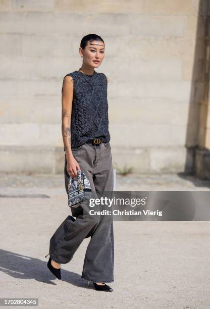 Amalie Gassmann wears grey sleeveless knit, grey denim jeans, belt, black white bag outside Dior during the Womenswear Spring/Summer 2024 as part of...
