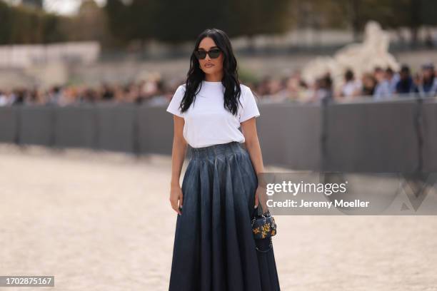 Amina Muaddi is seen wearing black sunglasses; silver hoop earrings; a white tee; a high-waisted, pleated, denim midi skirt with colour gradient and...