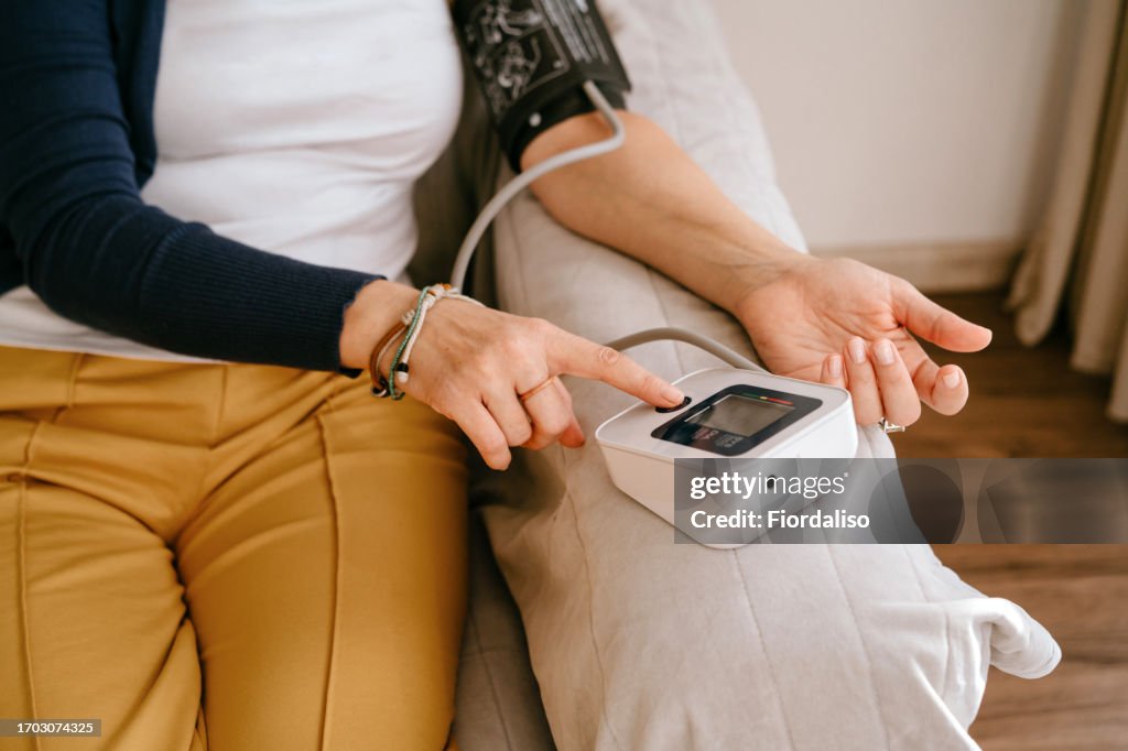 A middle-aged woman sitting on the sofa, using a tonometer to measure blood pressure