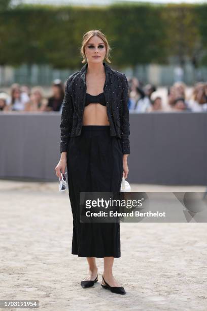 Olivia Palermo wears a black jacket with attached features, black bras, a midi pleated / gathered skirt, flat ballerina shoes, a white bag, outside...