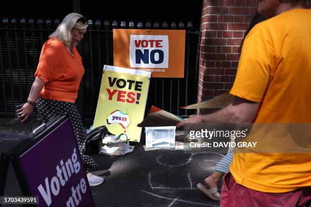 Woman walks past volunteers handing out voting brochures outside a voting centre in central Sydney on October 3, 2023. Early voting opened on October...