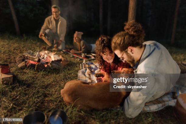 feliz pareja relajándose con su perro en el camping por la noche. - bonfire night food fotografías e imágenes de stock