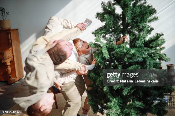 joyful father time: dad enjoys fun moments with sons while decorating set up christmas tree at bright cozy appartment - echte familie stock-fotos und bilder