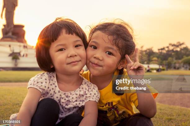 two little kids sitting on grass - sólo niñas fotografías e imágenes de stock