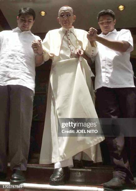 Influential Philippine church leader Cardinal Jaime Sin is helped by his aide after hosting a lunch for street children in Manila 29 August 2003 in...