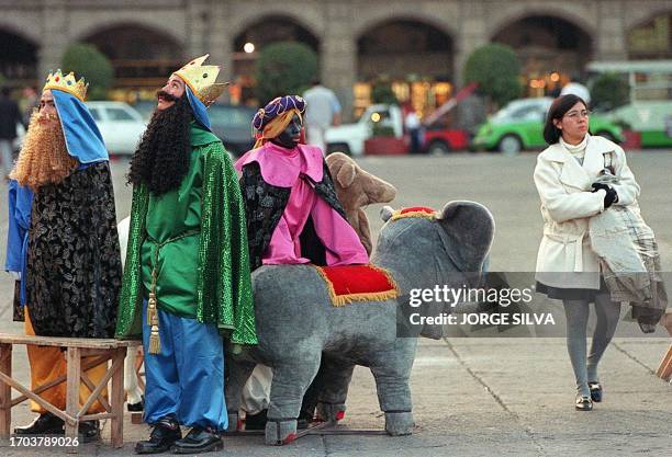 Woman walks through central Mexico City 05 January 2000 past three men dressed as the Magi for a traditional Catholic festival. Una mujer camina en...