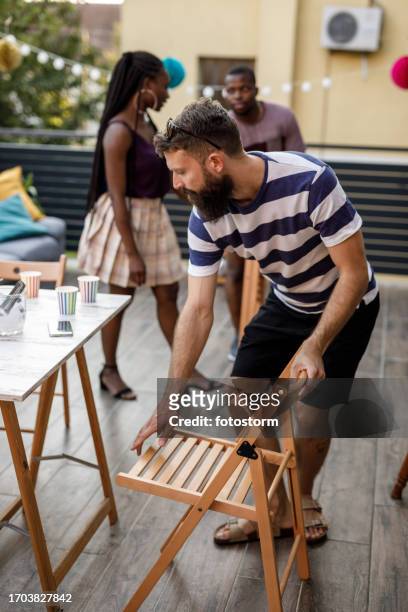 friends setting up fold up chairs around a table on the balcony for a party - the party arrivals stock pictures, royalty-free photos & images
