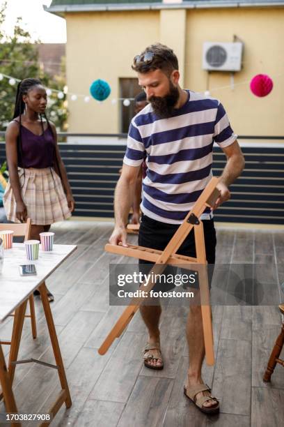 friends setting up fold up chairs around a table on the balcony for a party - the party arrivals stock pictures, royalty-free photos & images