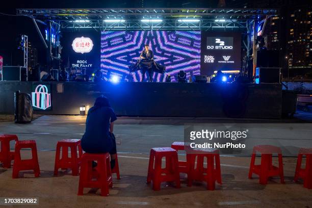 Women sitting on a chair watching a DJ performing on stage at a pop up night market in wan chai promenade on October 2, 2023 in Hong Kong, China. The...