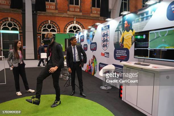 British Prime Minister Rishi Sunak watches a man using a VR headset at an FA stand at the Exhibitor's Hall on Day 3 of the Conservative Party...