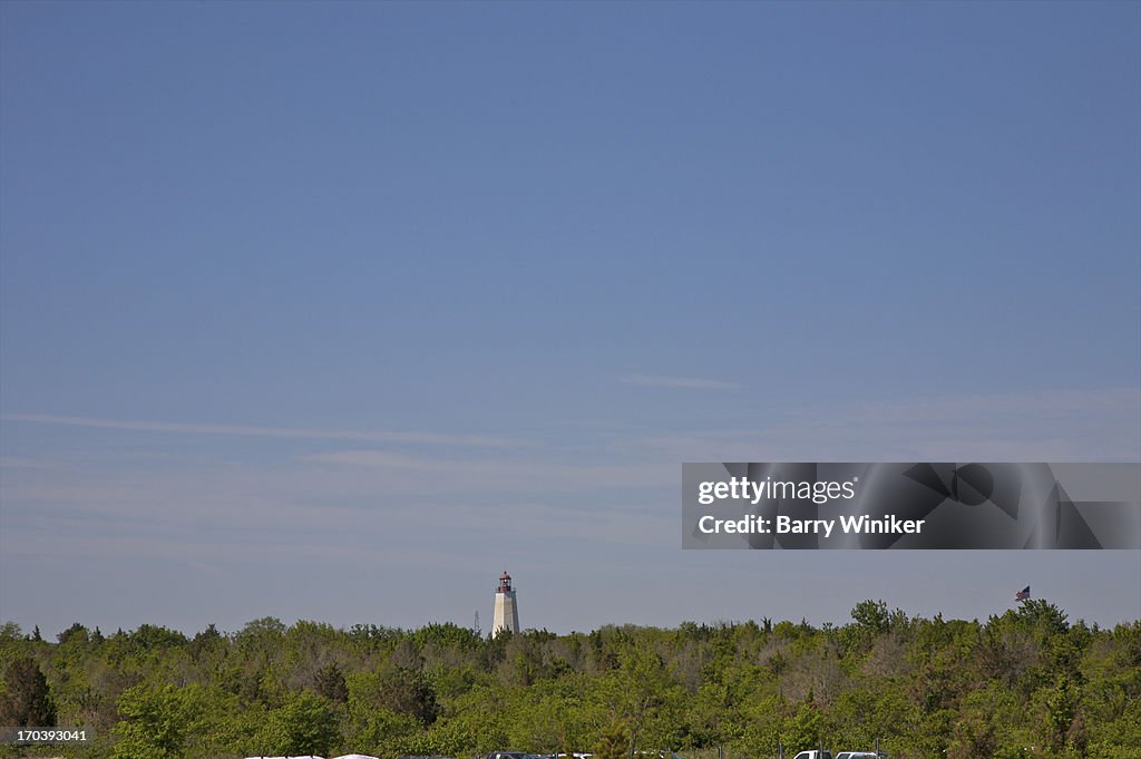 Lighthouse peeking above tree line under blue sky