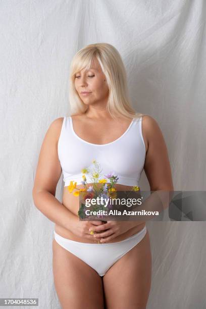 self acceptance, love and care. smiling curvy woman with flowers bouquet posing in underwear isolated on grey studio background. self esteem concept - chesty love stock pictures, royalty-free photos & images