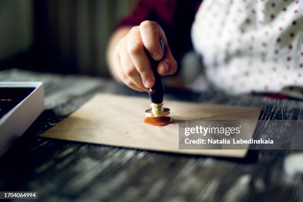 close-up sealing process: a woman's hand takes center stage as she uses sealing wax and a wax seal to close a brown paper envelope. - stempel büromaterial stock-fotos und bilder