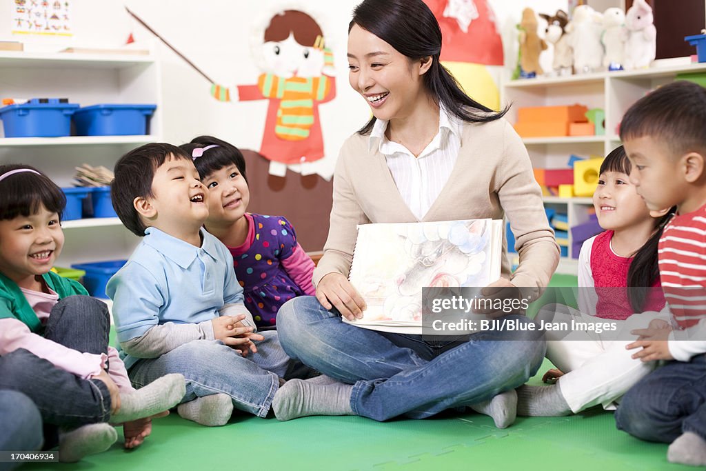 Female teacher showing kindergarten children picture book