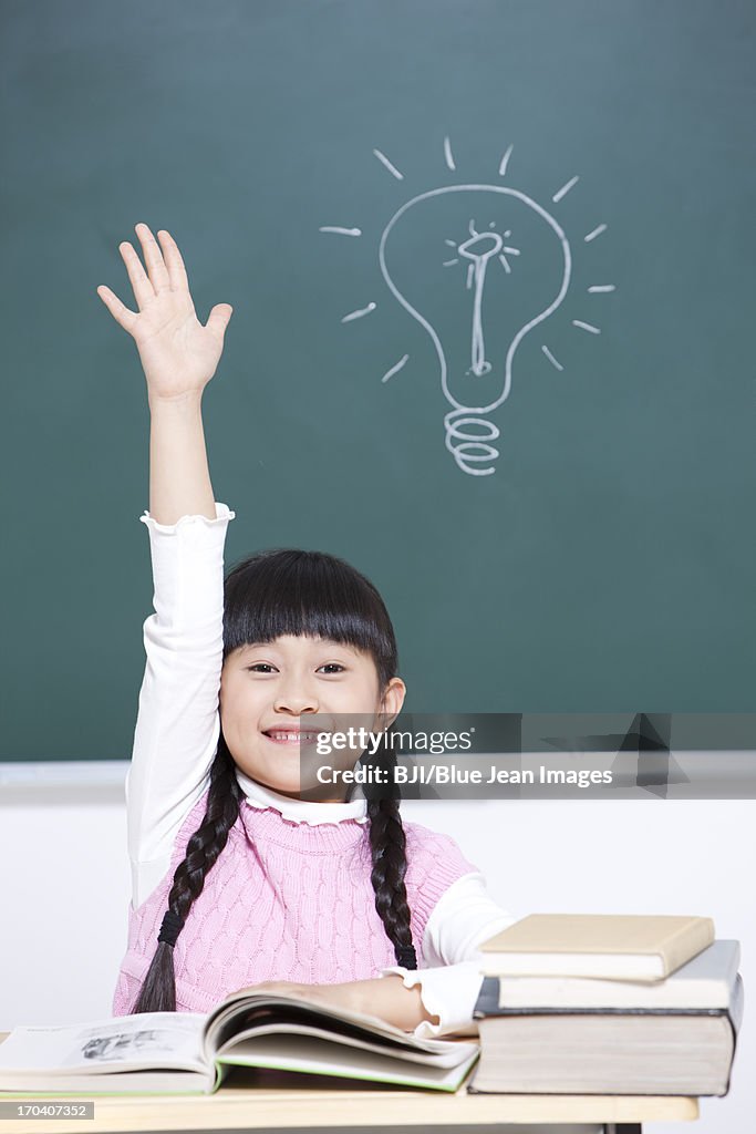 Cheerful schoolgirl raising hand in classroom