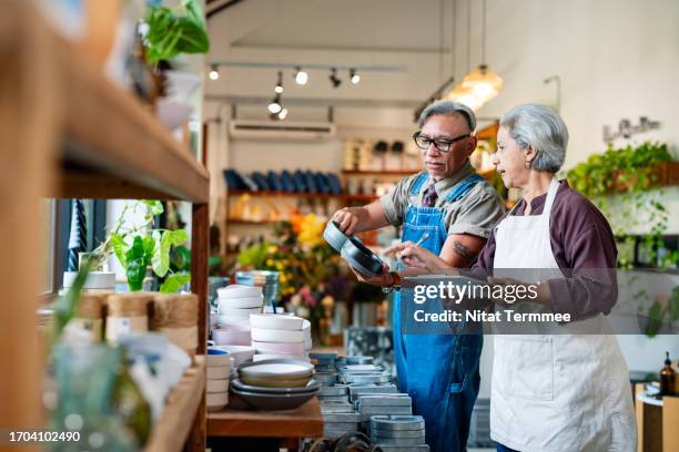 product quality is important for your business. proud of senior male and female asian small business owners check and confirm the quality of kitchenware handmade on a display shelf inside their shop. - duurzaam consumeren stockfoto's en -beelden
