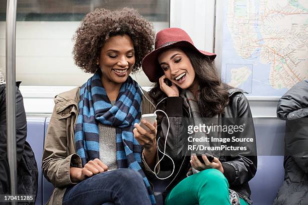 women sharing earphones on subway - sharing headphones stock pictures, royalty-free photos & images