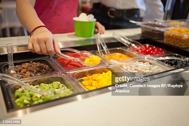 girl putting toppings on frozen yogurt - frozen yoghurt stock pictures, royalty-free photos & images