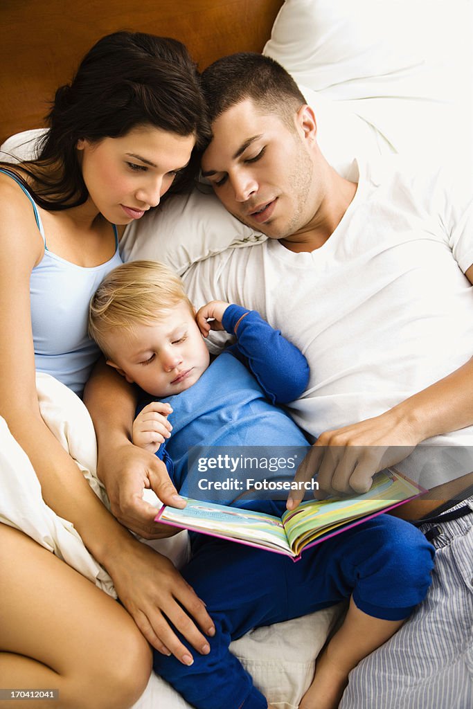 Parents and son reading book in bed