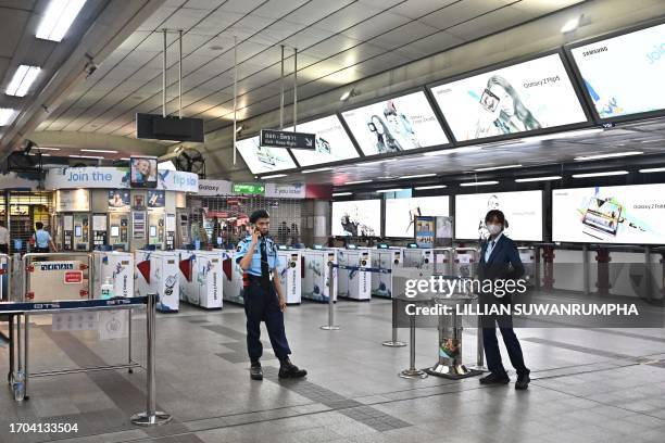 Employees stand at a closed exit of a BTS train station near Siam Paragon mall in downtown Bangkok on October 3, 2023. Hundreds of people fled a...