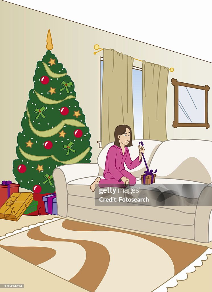 Girl in pajamas on couch opening a Christmas present