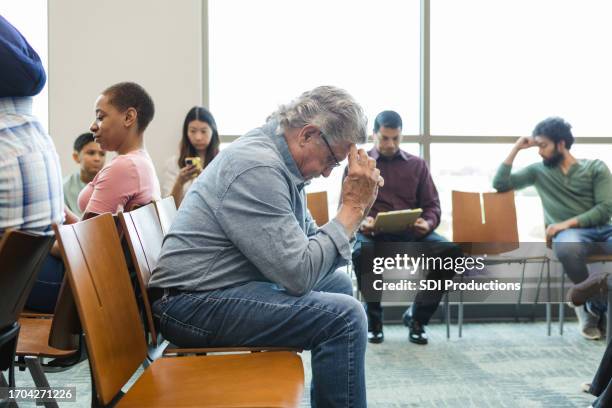 senior adult man sits in the waiting room with his head in his hands - hospital waiting room stockfoto's en -beelden