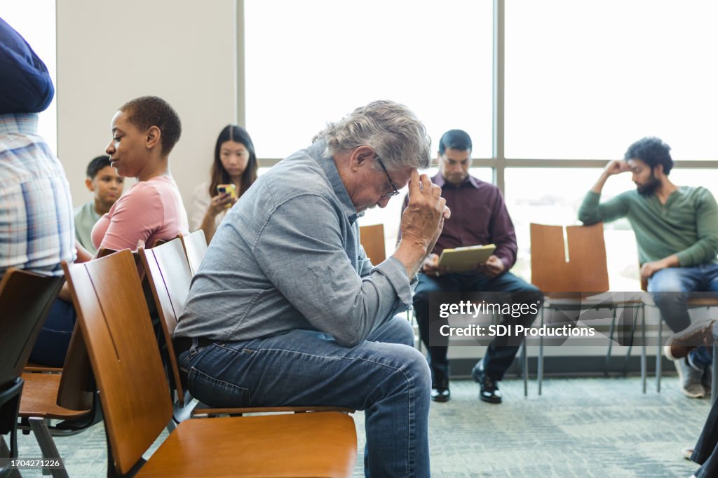 Senior adult man sits in the waiting room with his head in his hands